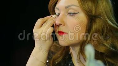化妆室里的红发女演员用银色的影子做眼妆，准备上台